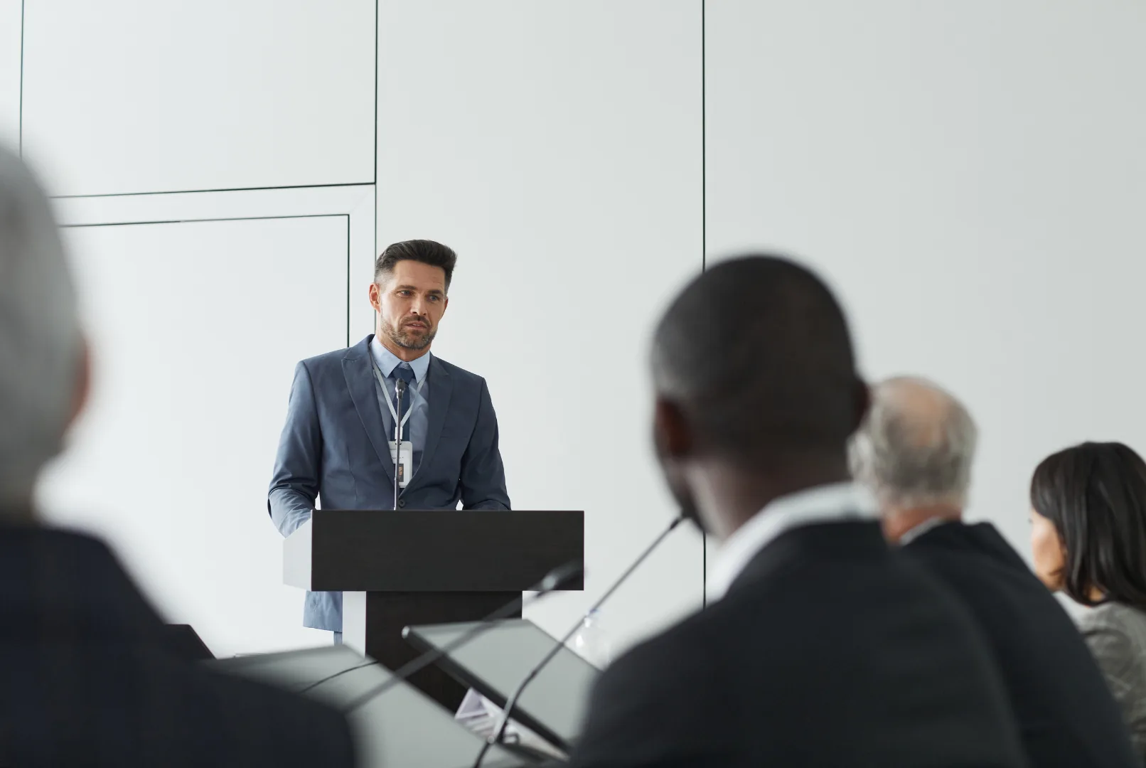 A speaker at a podium seen past the backs of seated attendees' heads